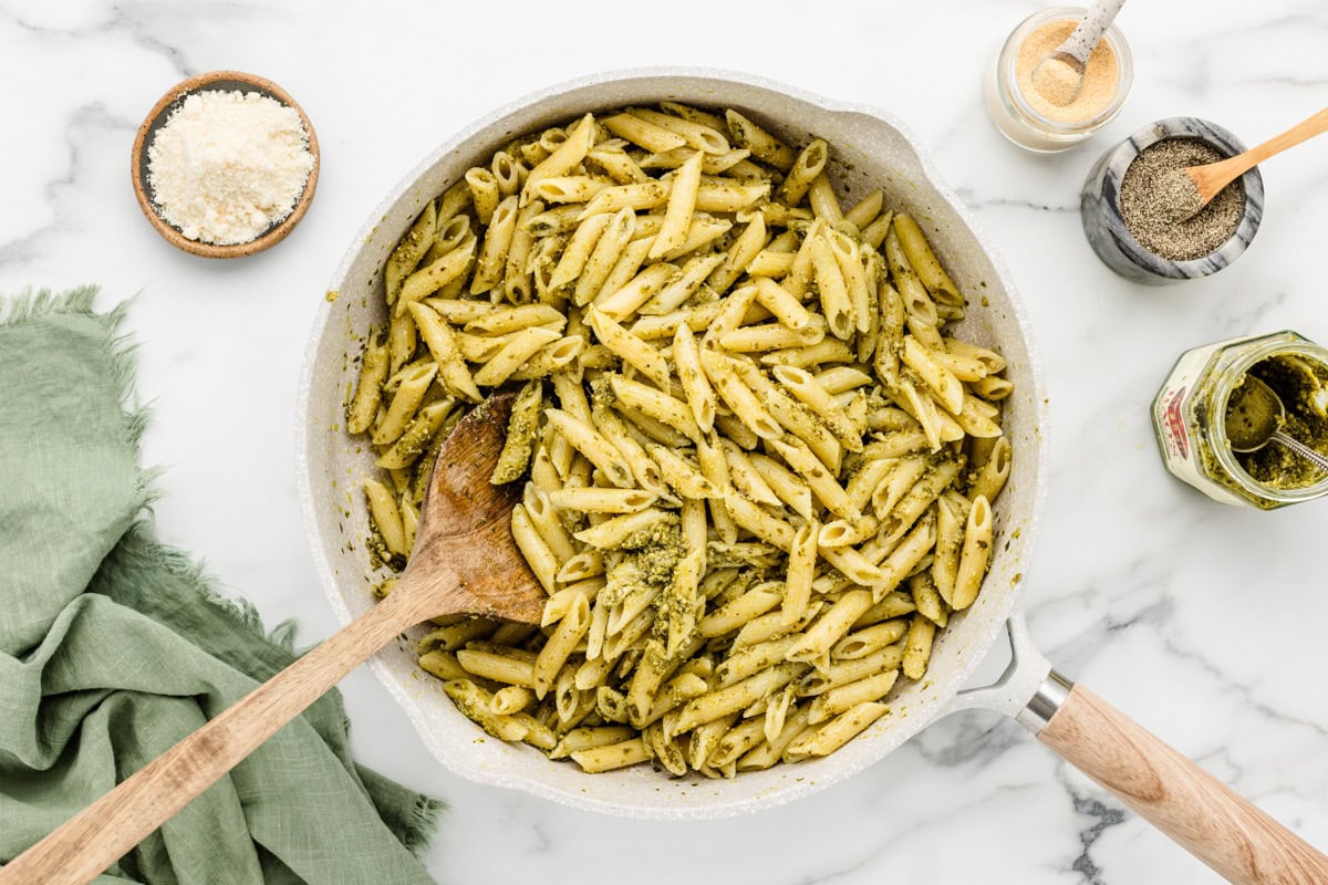 Mixing pesto with cooked pasta in a skillet.