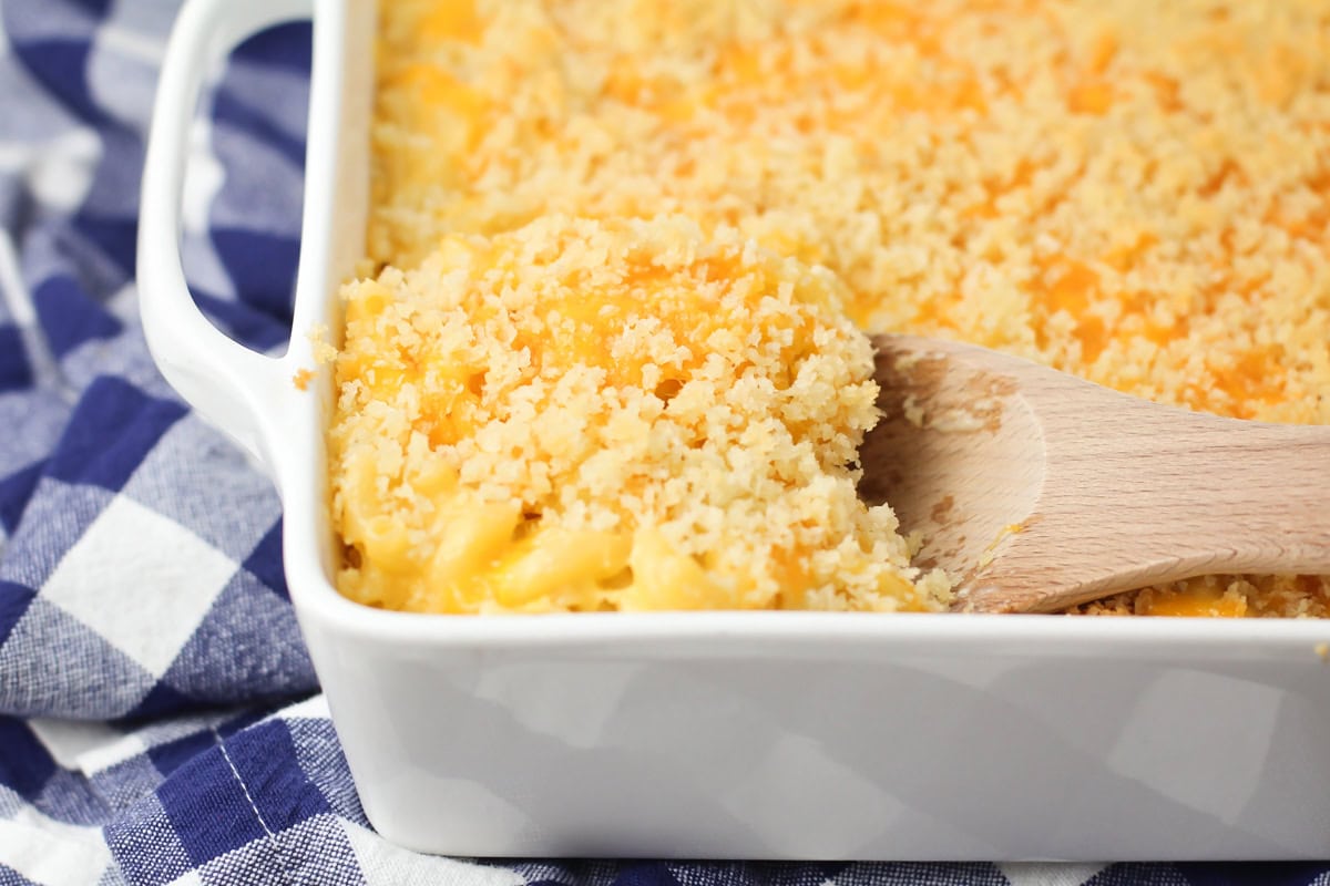 A close up of a wooden spoon scooping velveeta mac and cheese bake from a white baking dish.