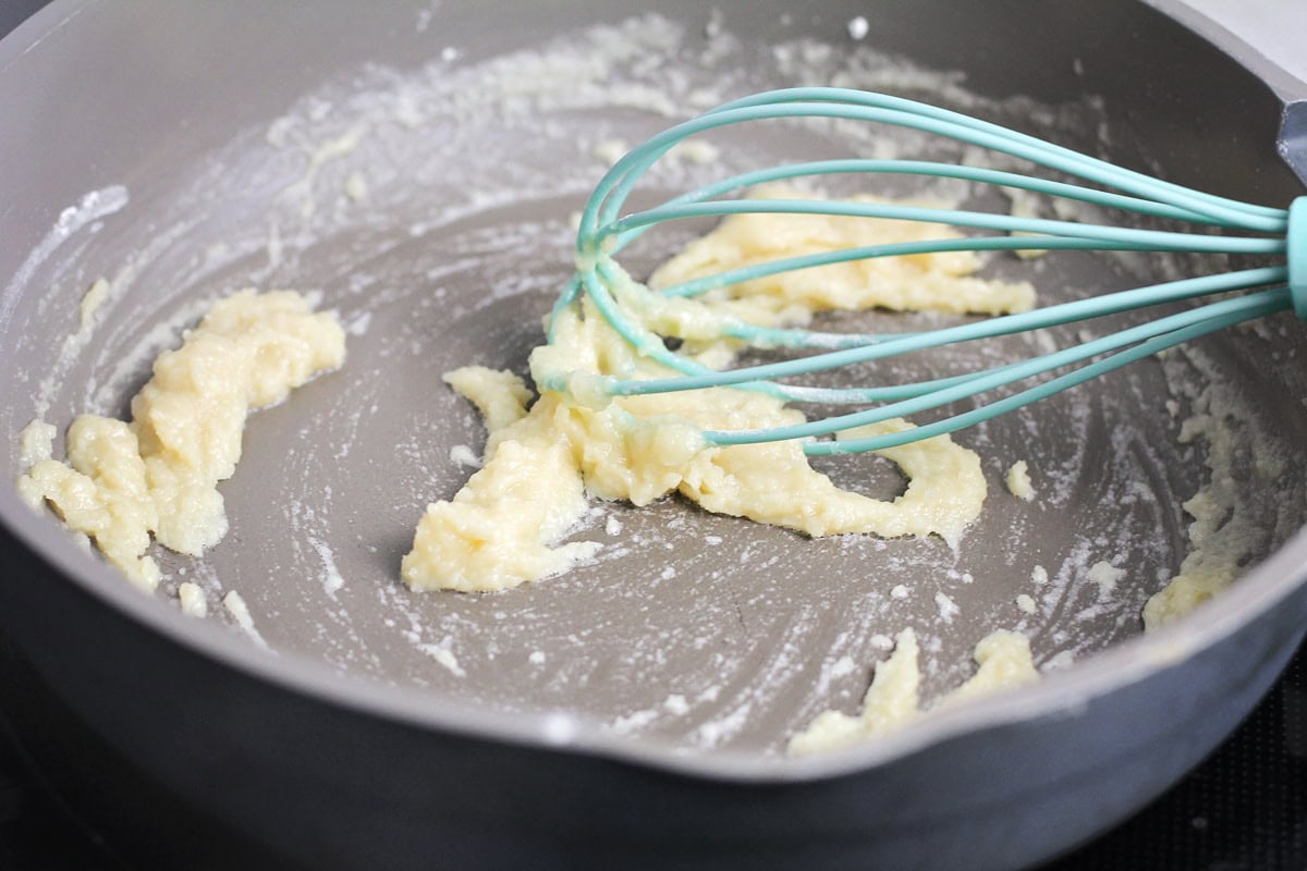 Whisking flour and butter to make a roux in a pan.