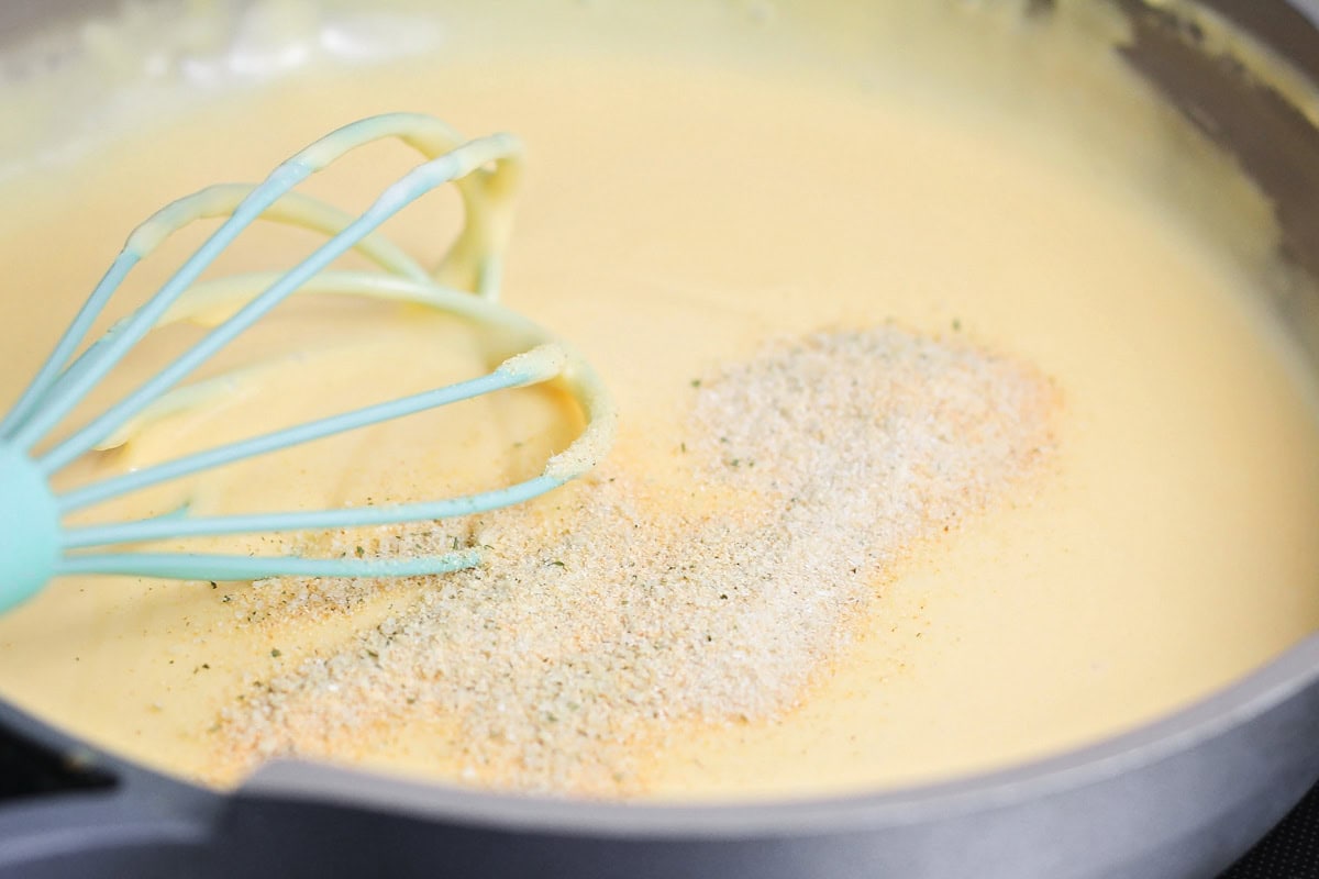 Whisking seasonings into a cheese sauce in saucepan.