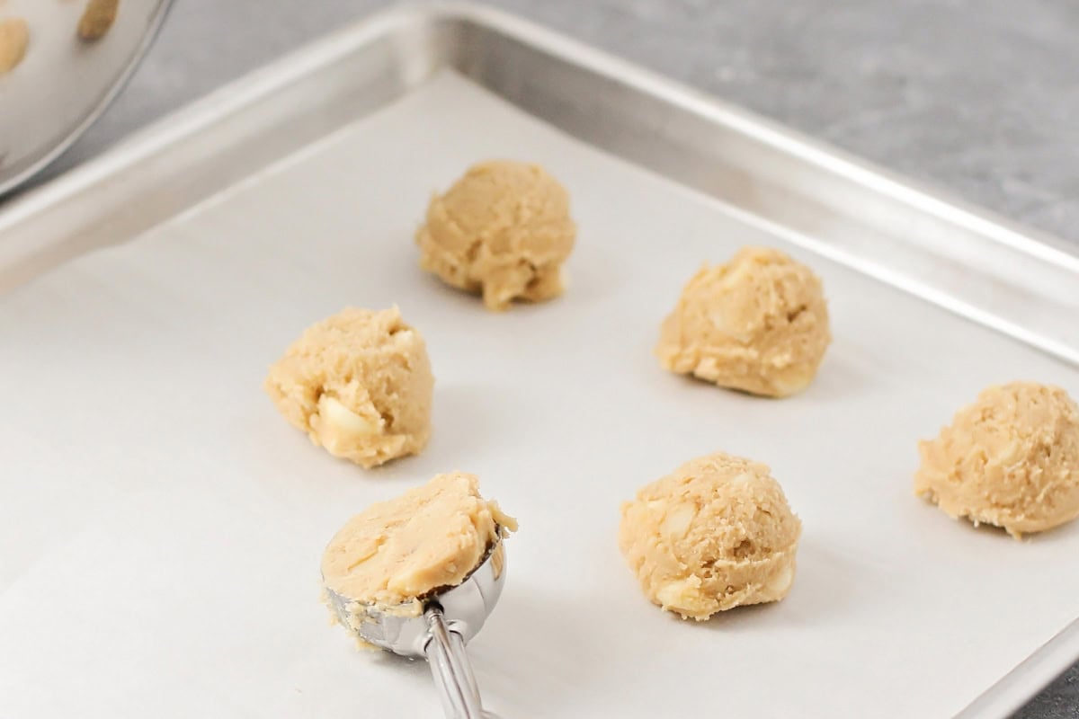 Scooping cookie dough onto a lined baking sheet.