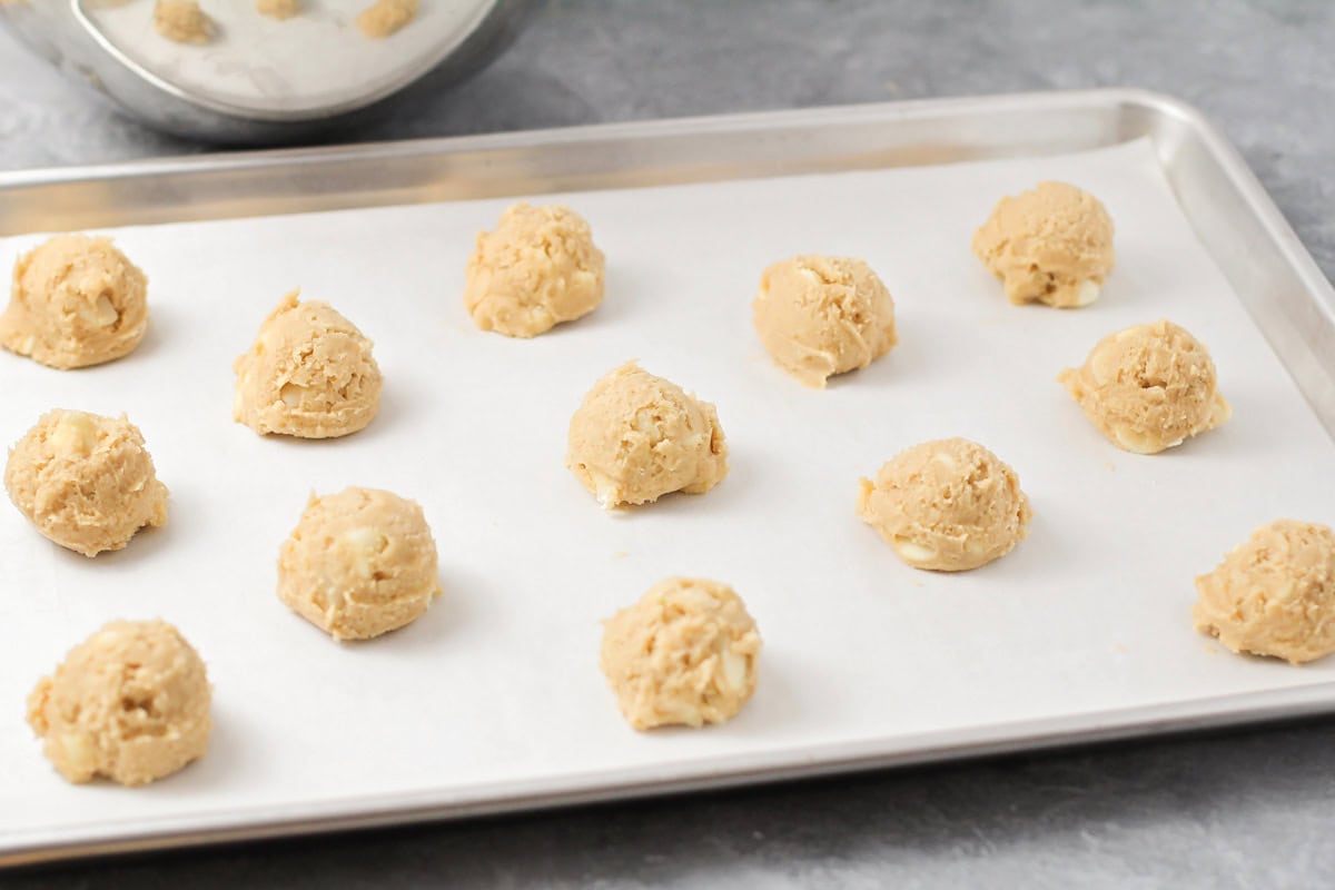 Cookie dough balls on a lined baking sheet.