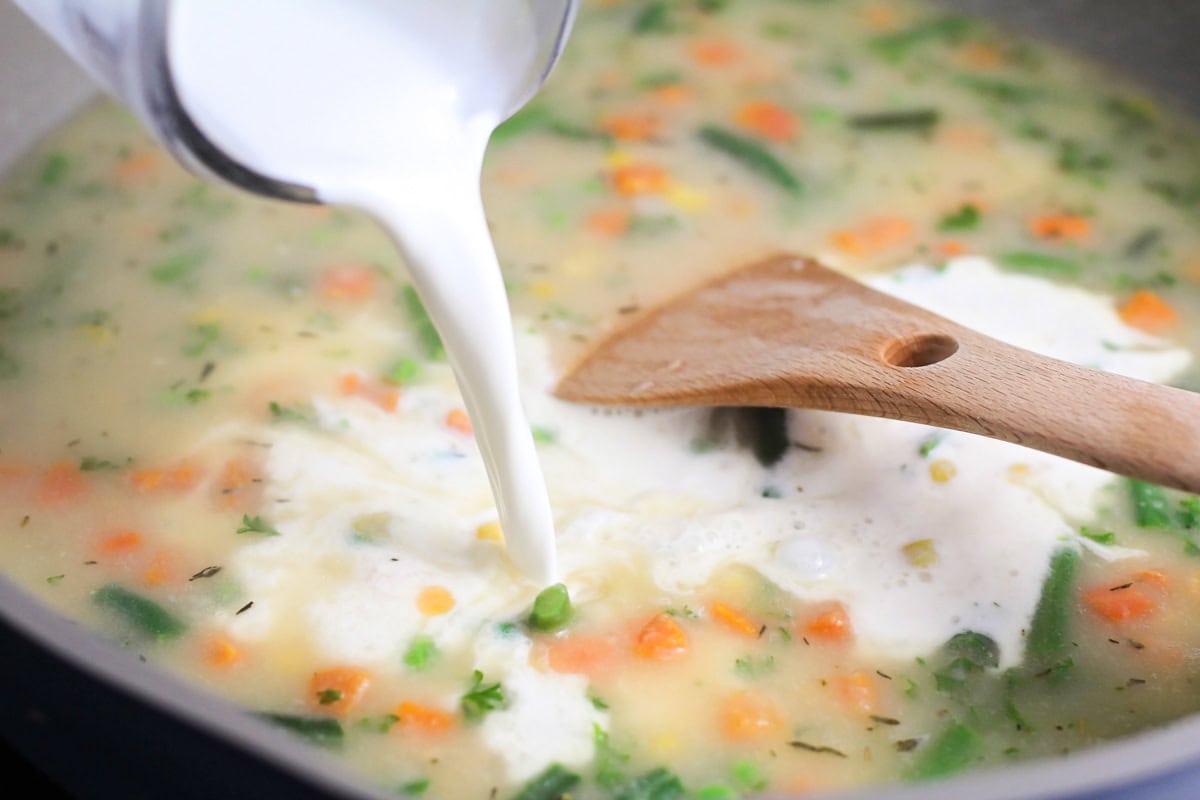 Cream being added to veggies in pan.