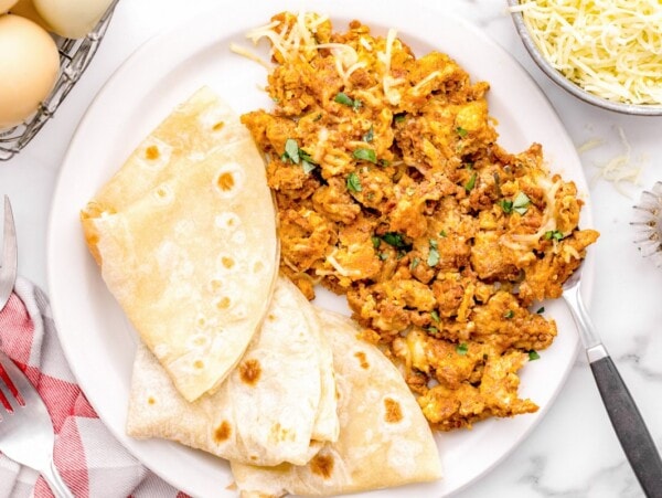 Chorizo and eggs served with tortillas on white plate.