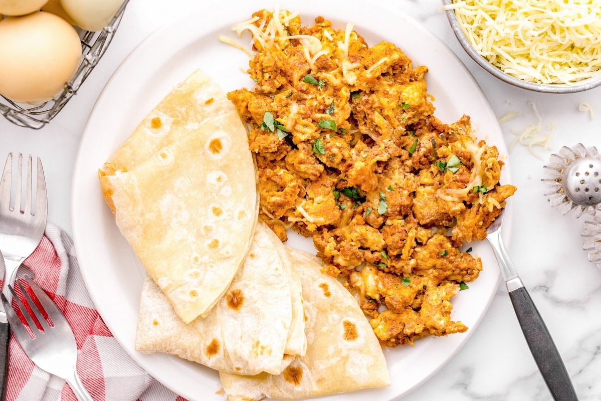 Chorizo and eggs with flour tortillas on a white plate.