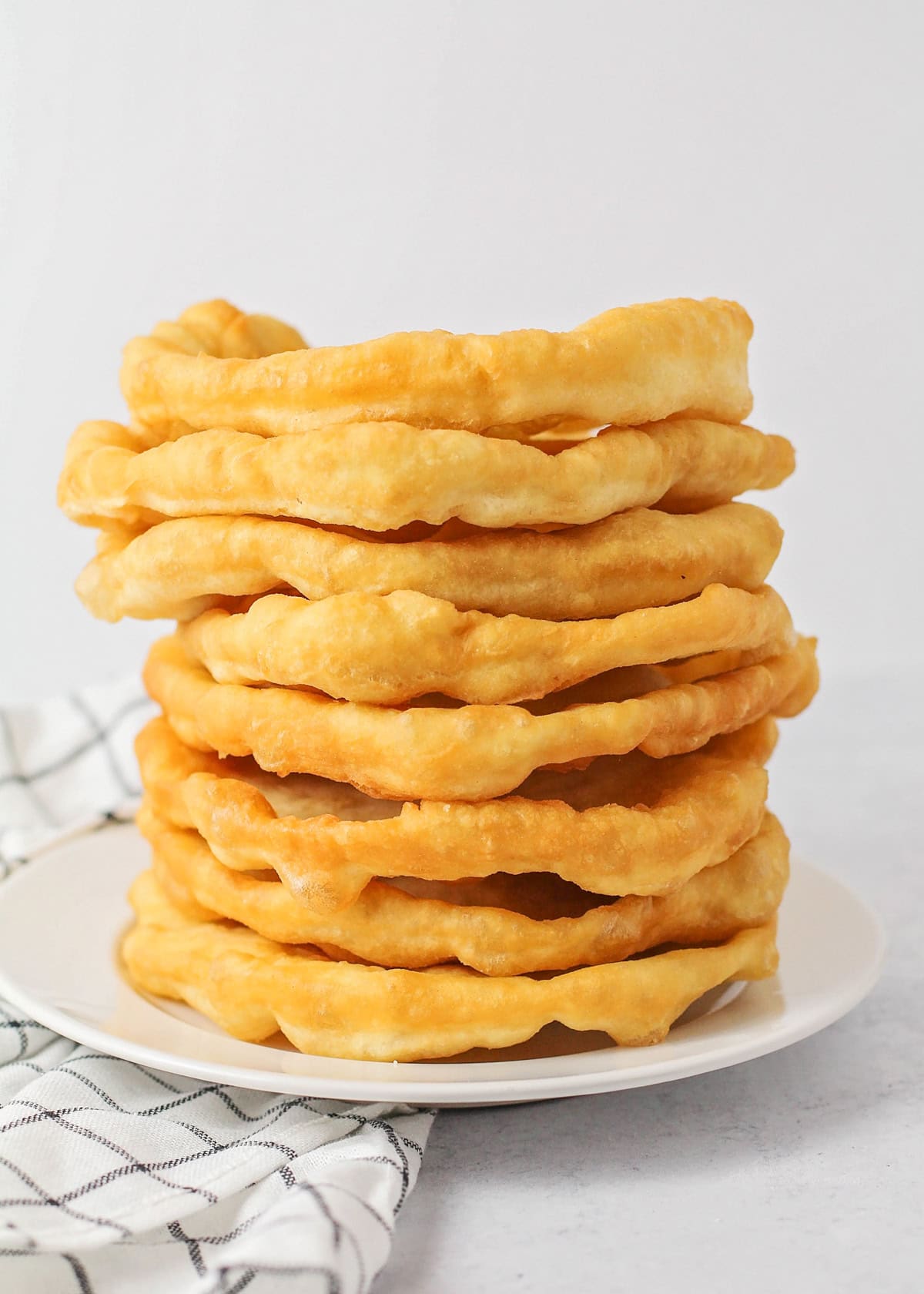 Homemade fry bread stacked on top of each other on white plate.