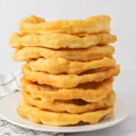 Homemade fry bread recipe all stacked on top of each other on white plate.