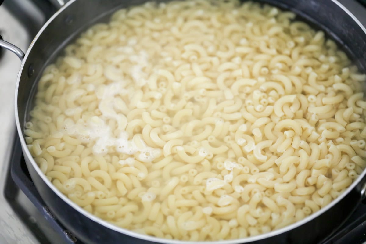 Elbow macaroni cooking in pot with water for macaroni salad recipe.