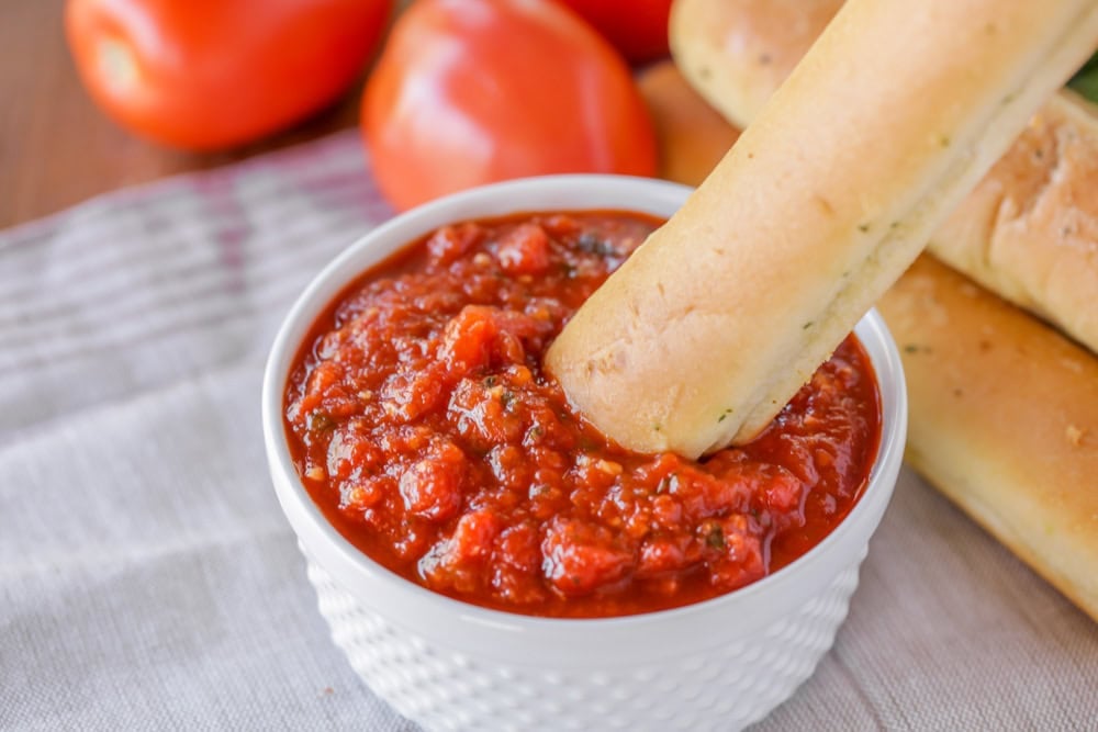 This simple homemade marinara sauce simmers fresh tomatoes with fragrant herbs and garlic for a versatile flavor explosion. Dipping a breadstick into homemade marinara sauce.