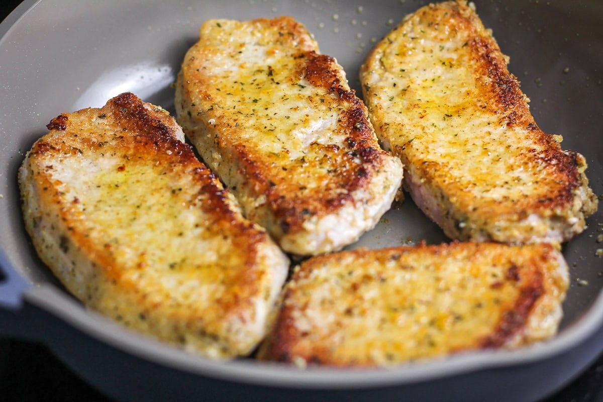 Pork chops with a parmesan crust cooking in skillet.