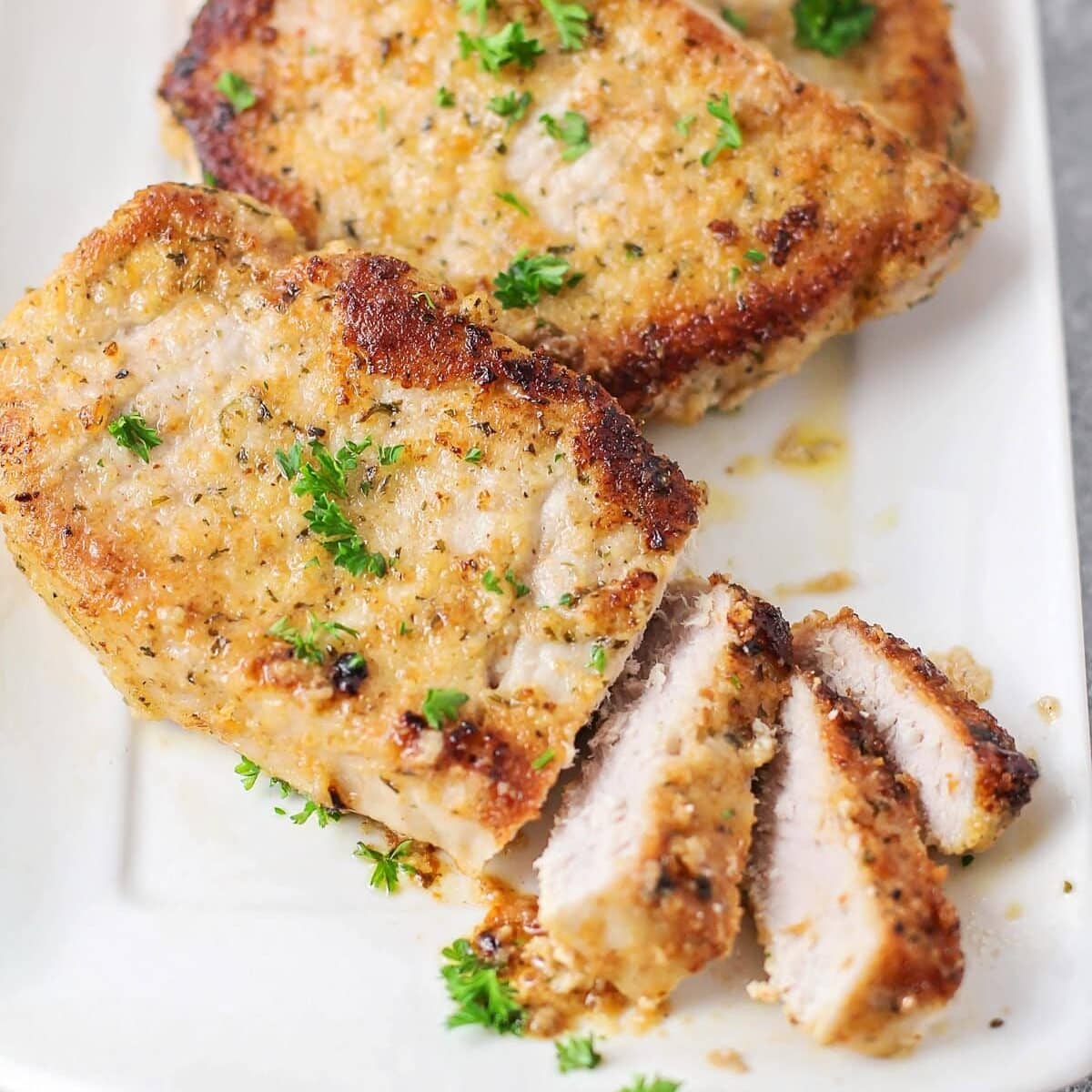 Parmesan Crusted pork chops close up image - cut up on white plate.