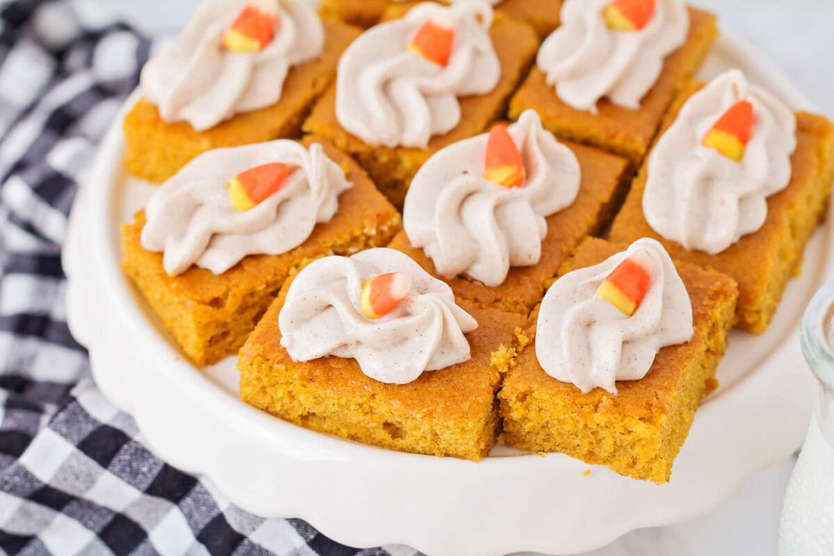 Fall flavors explode in these moist pumpkin bars, boasting a decadent swirl of cinnamon cream cheese frosting! Multiple pumpkin bars on a white plate.