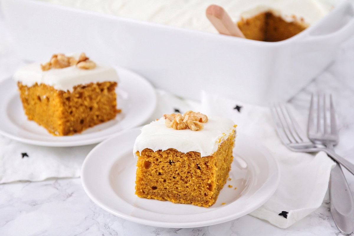 A slice of pumpkin cake topped with chopped walnuts served on a white plate.