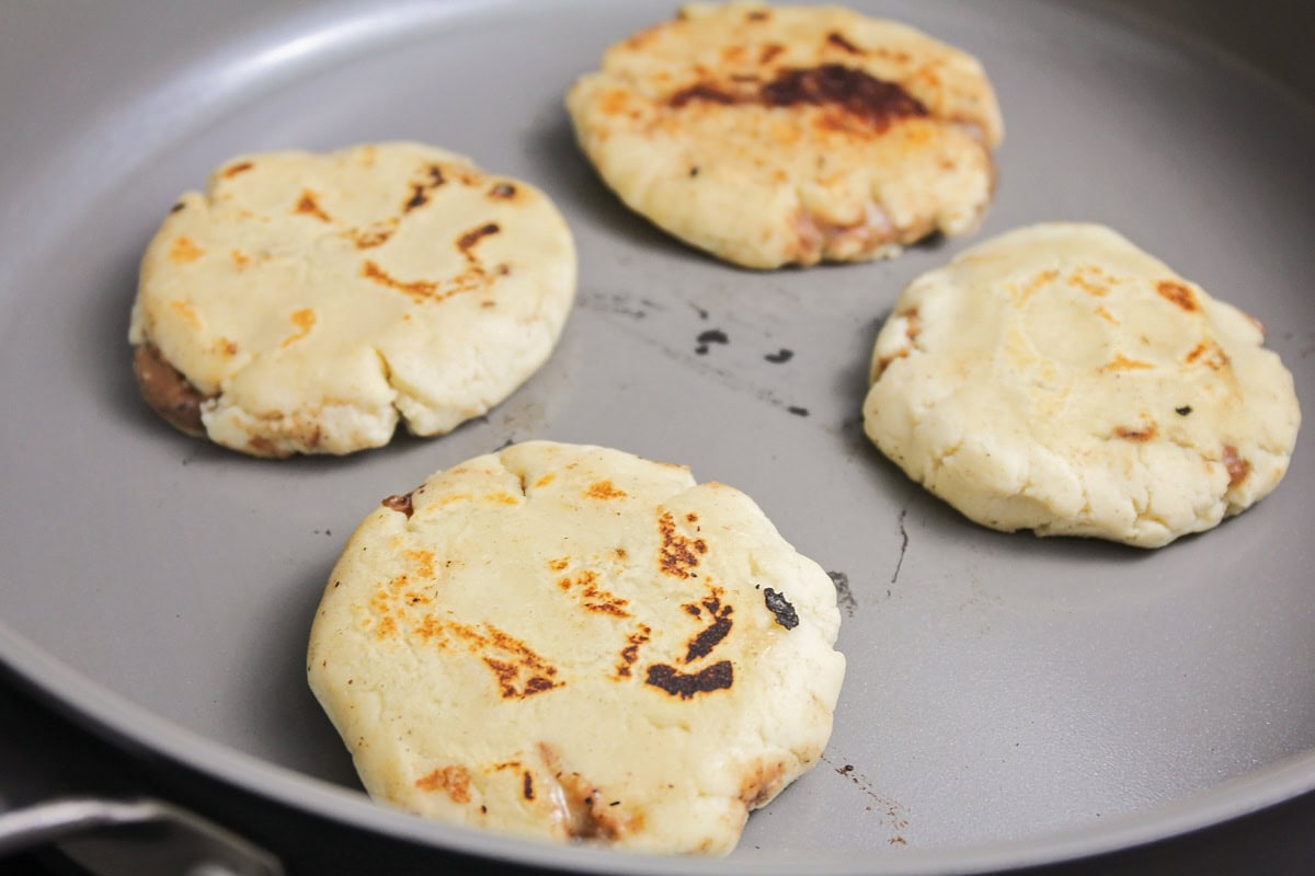 Pupusas being fried in skillet.