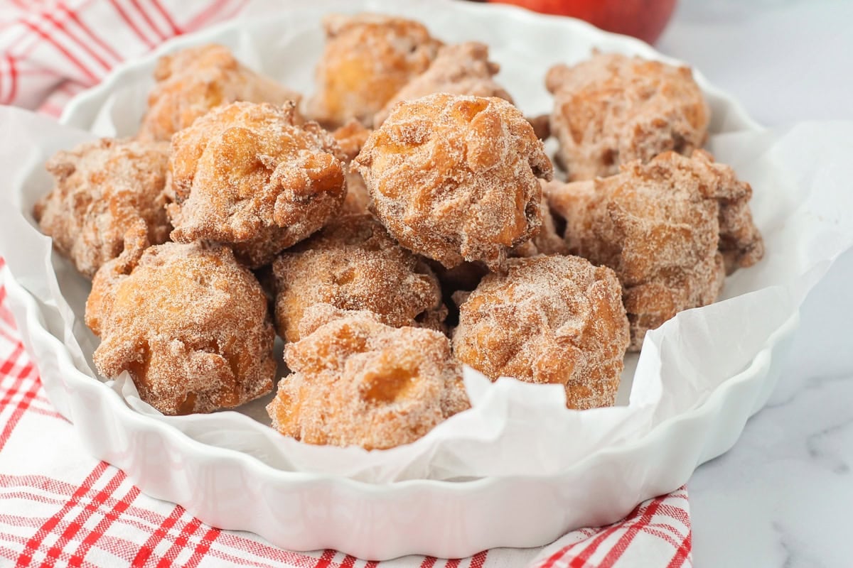 A pile of apple fritters in a white serving dish.