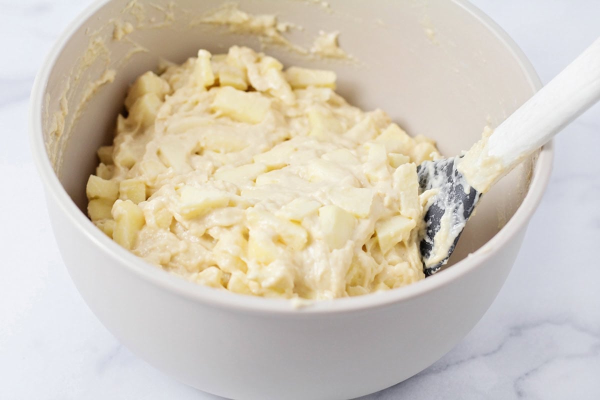 Mixing apple chunks into a fritter batter.