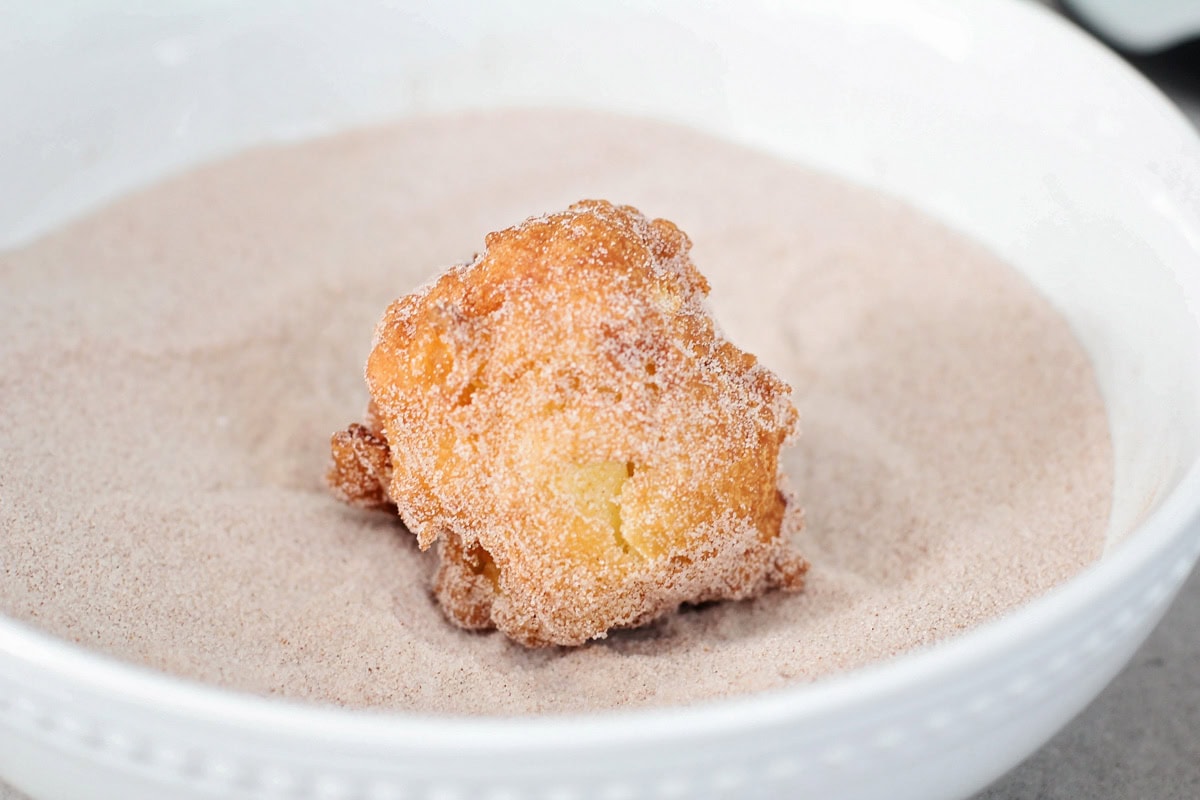 Fried apple fritter being tossed in cinnamon and sugar.