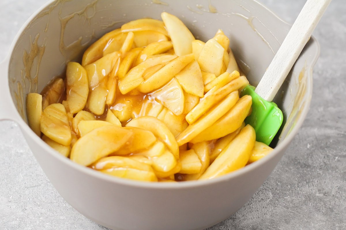 Mixing sliced apples in sauce in a bowl.