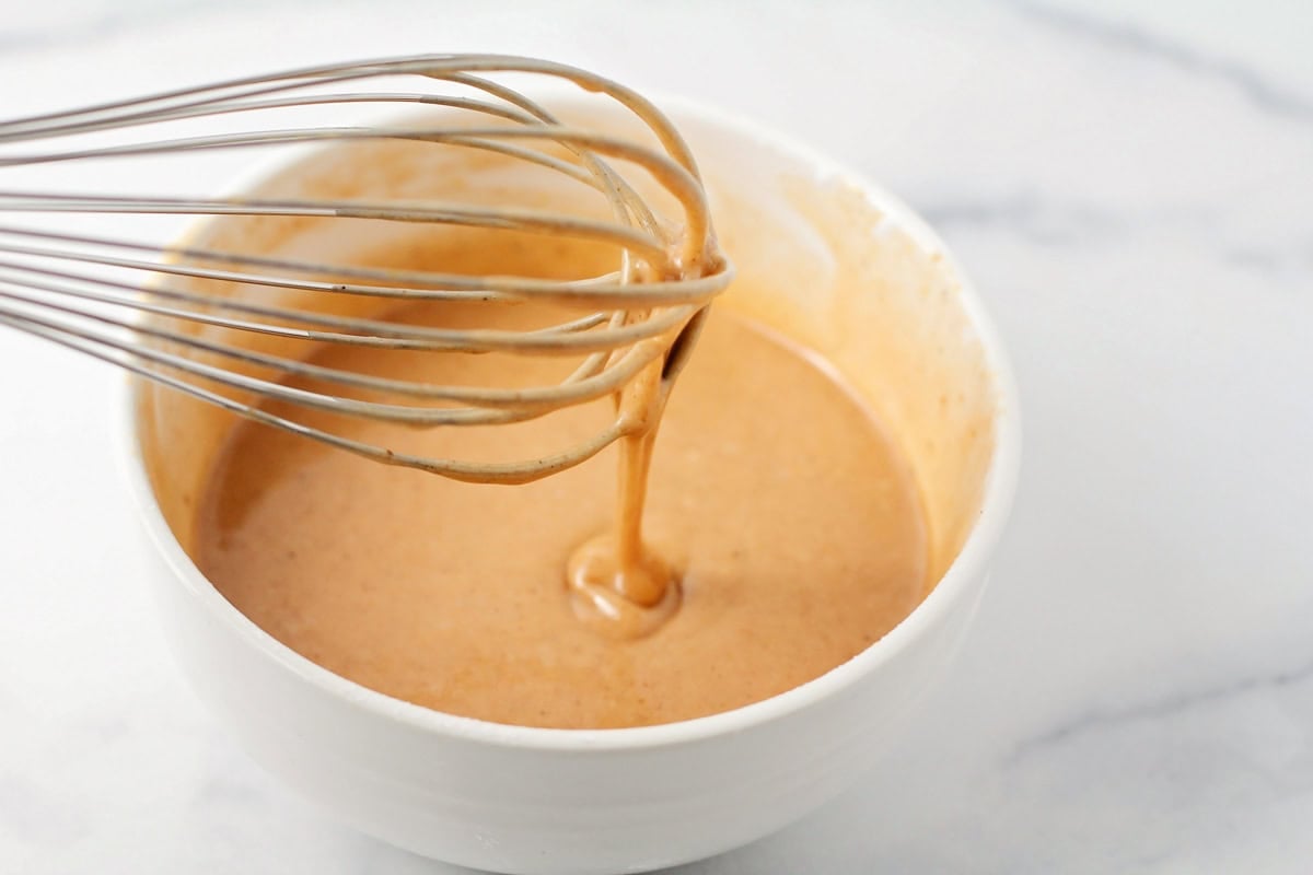 Whisking a pumpkin glaze in a white bowl.