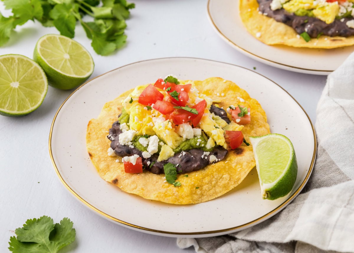 A breakfast tostada served on a plate with a lime wedge.