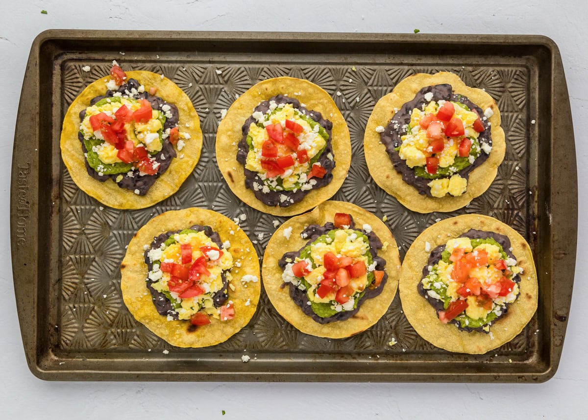 Adding diced tomatoes to the top of the tostadas.