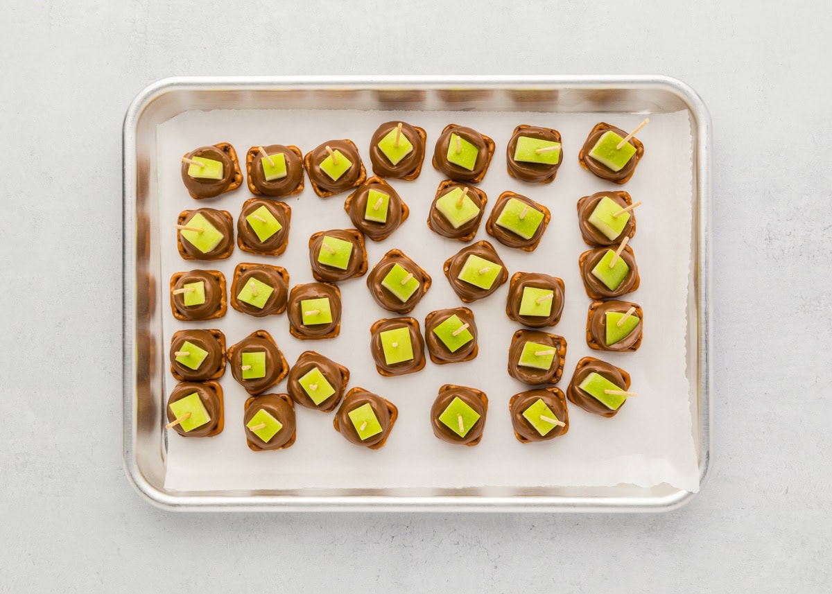 Several caramel apple bites on a lined baking sheet.