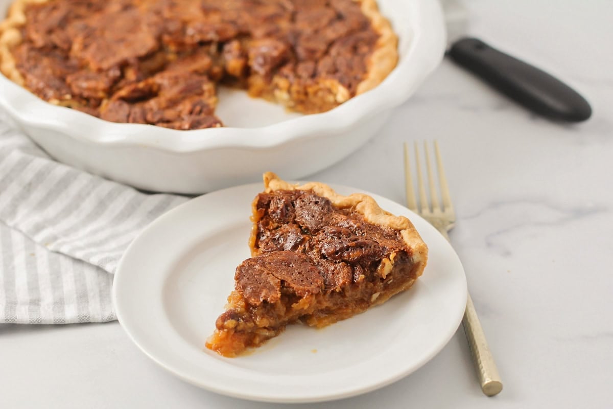 A slice of caramel pecan pie on a white plate.