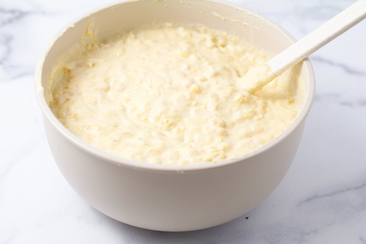 Corn, sour cream, and corn bread mixture combined in a white bowl.