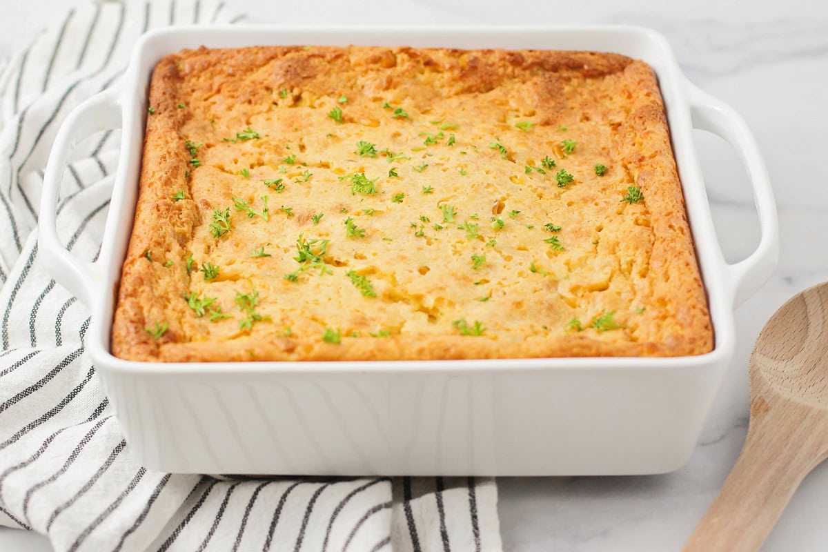 Corn souffle in a white square baking dish.