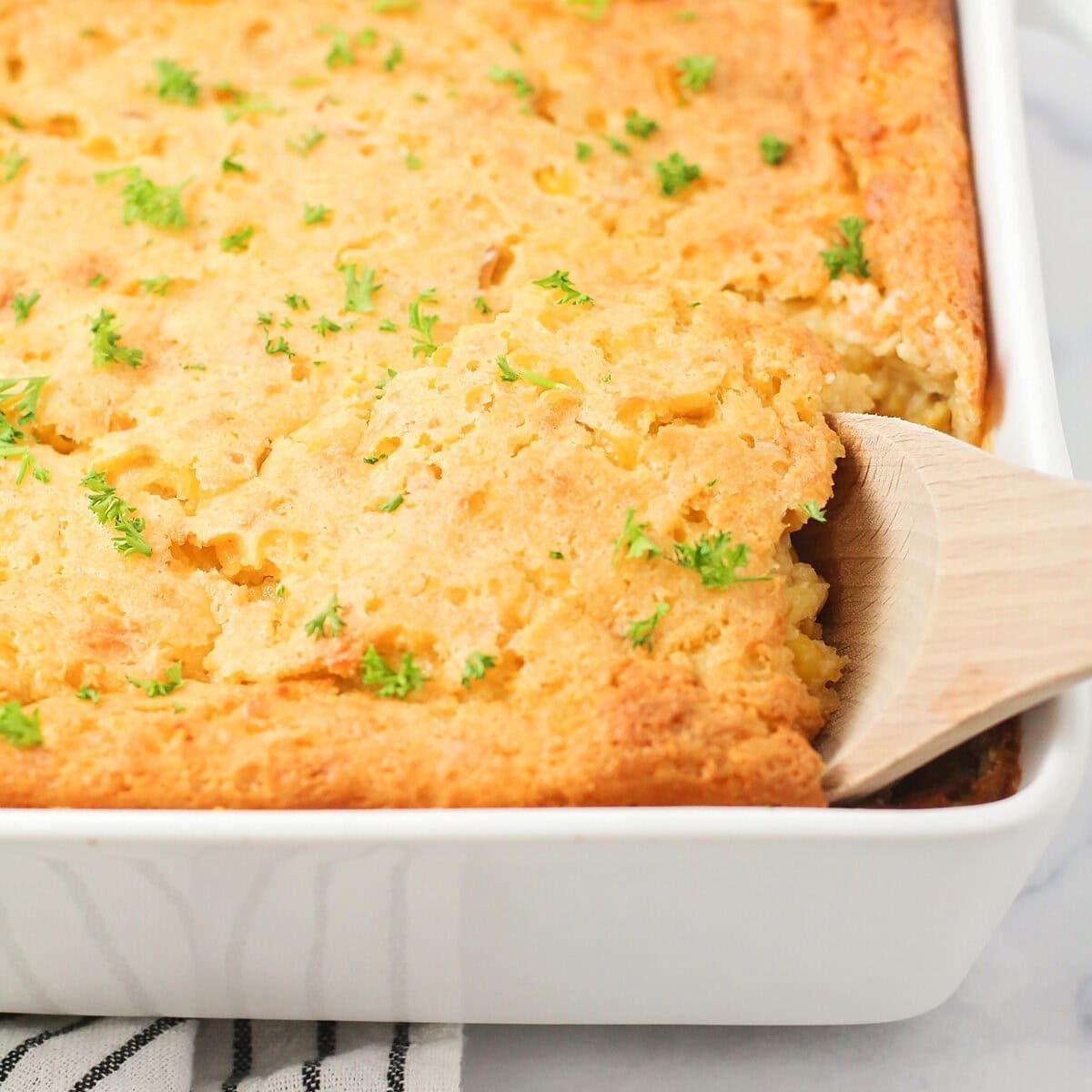 Scooping corn souffle from a white baking dish.