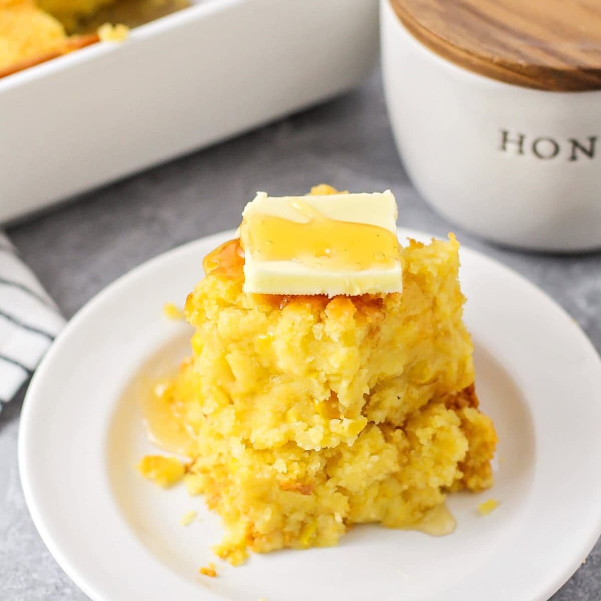 Close up image of two pieces of cornbread casserole on top of each other on white plate.