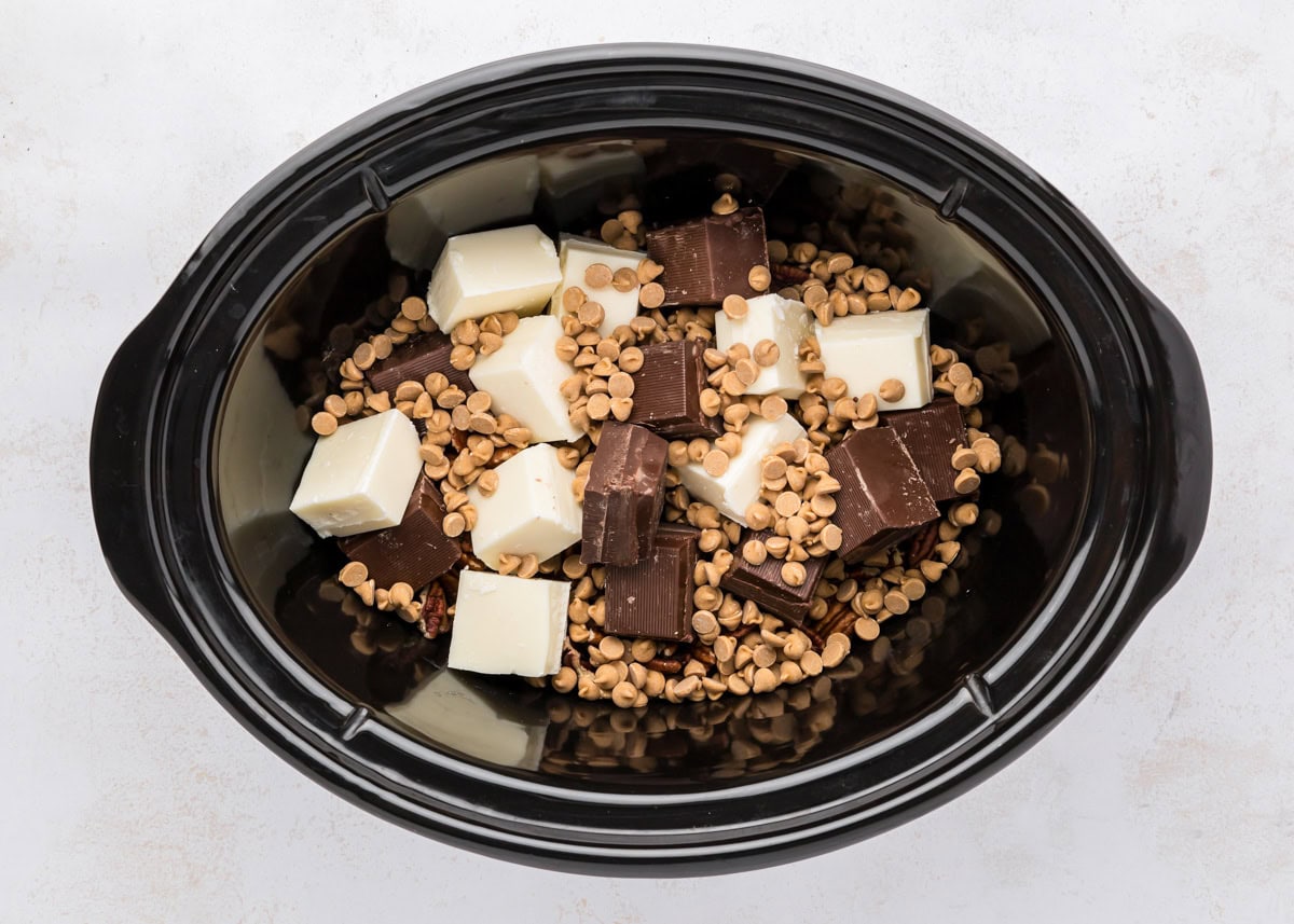 Adding chocolate and peanut butter chips to a slow cooker.