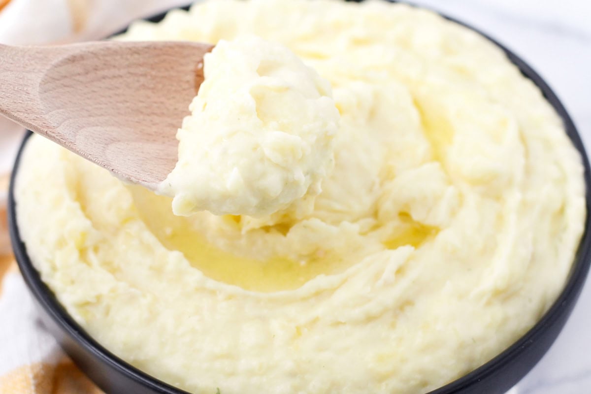 Scooping garlic mashed potatoes from a black bowl with a wooden spoon.