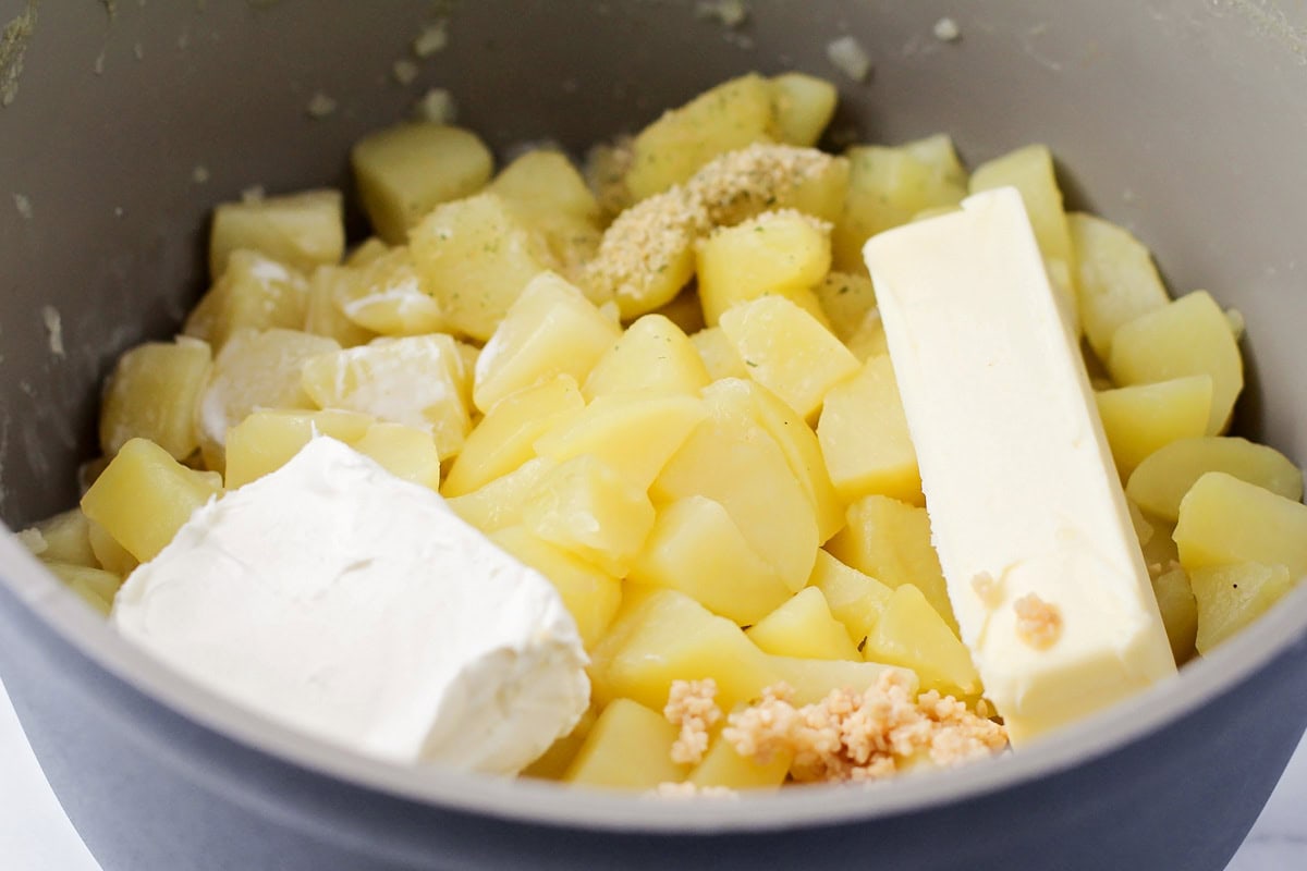 Adding butter and seasonings to a pot of cooked, cubed potatoes.