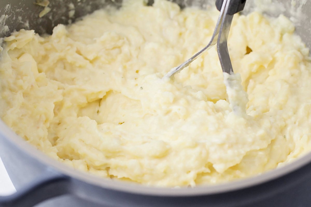 Mashing potatoes and seasonings in a pot.