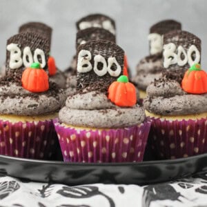 Halloween cupcakes decorated on plate with mallow pumpkin and Graveyard cookie.