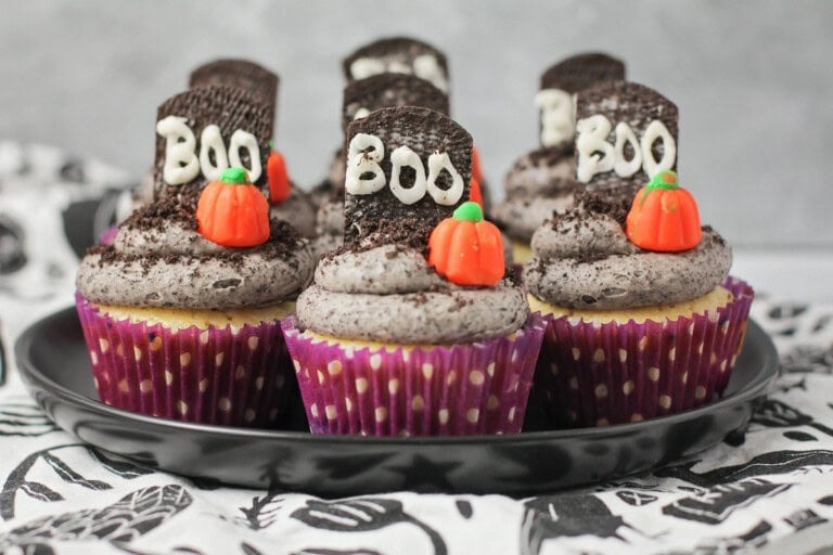 Halloween cupcakes decorated on plate with mallow pumpkin and Graveyard cookie.