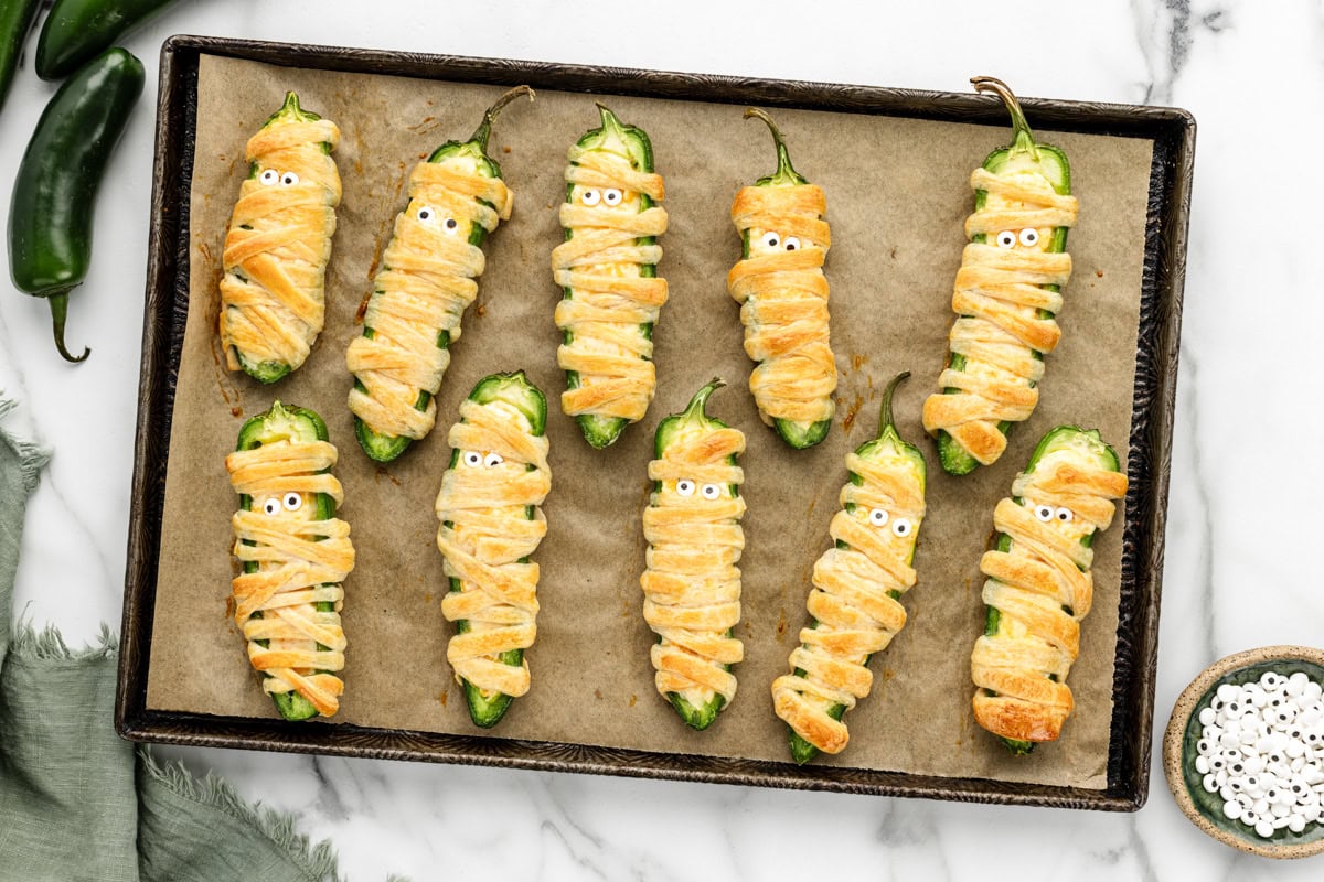 Jalapeno popper mummies with candy eyes on a baking sheet.