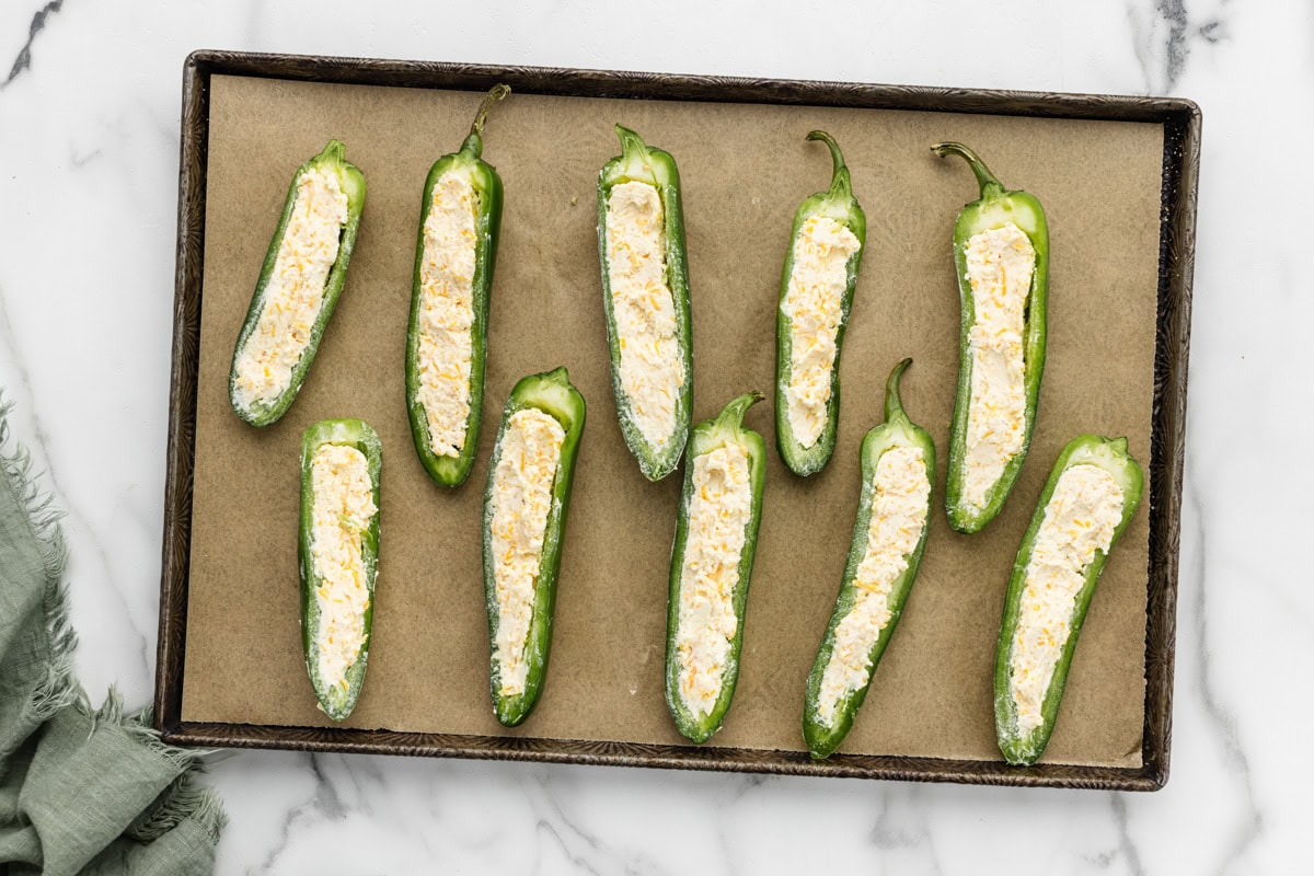 Jalapenos filled with cream cheese on a baking dish.