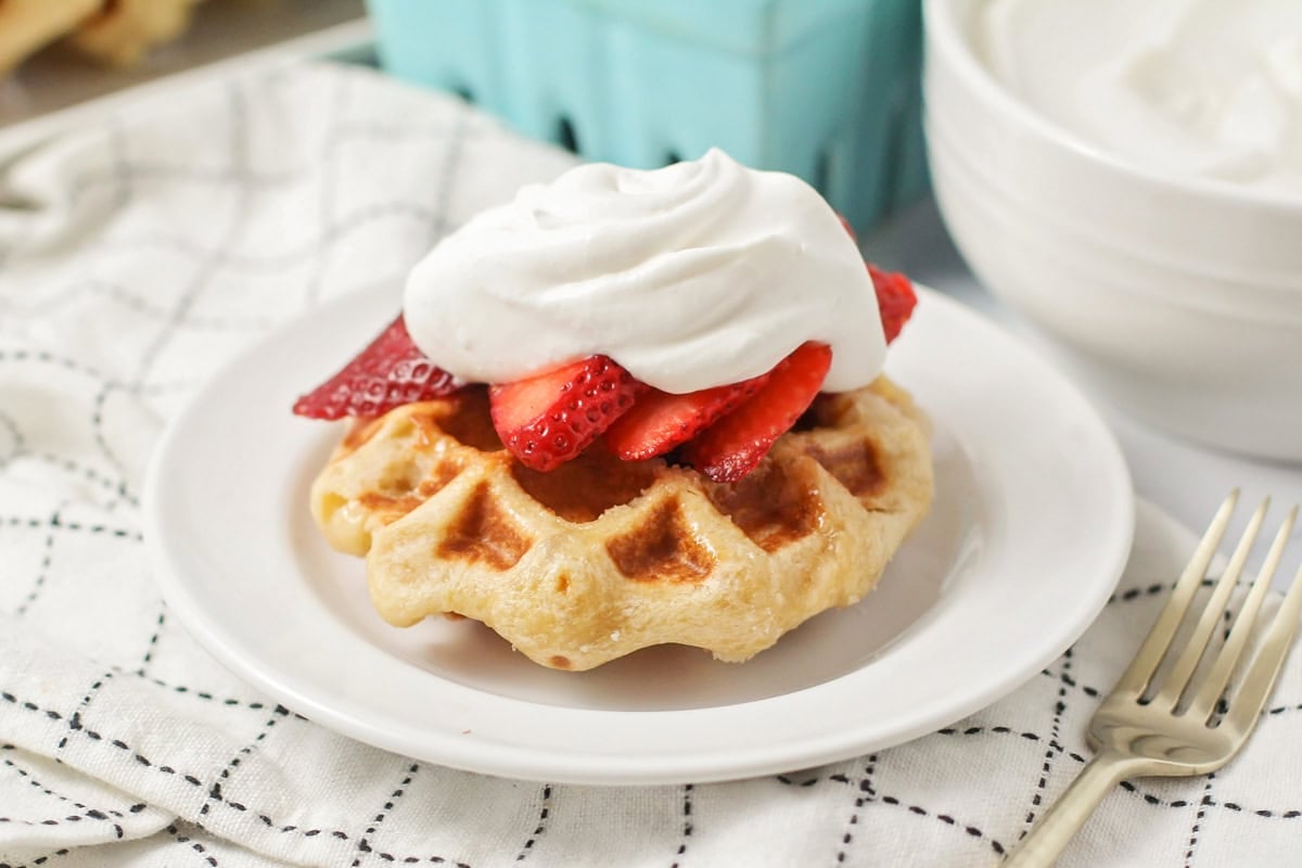 Liege waffles topped with sliced fresh strawberries and whipped cream.