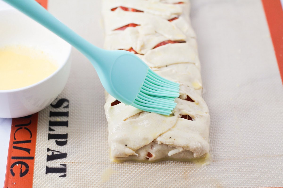 Brushing crescent dough with egg mixture and prepping to bake.