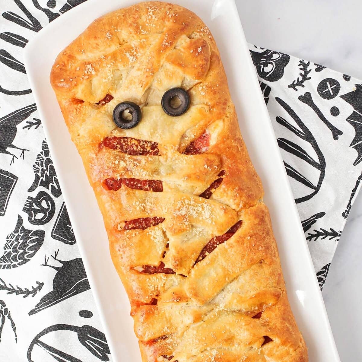 A crescent mummy pizza with two olive eyes on a white platter.