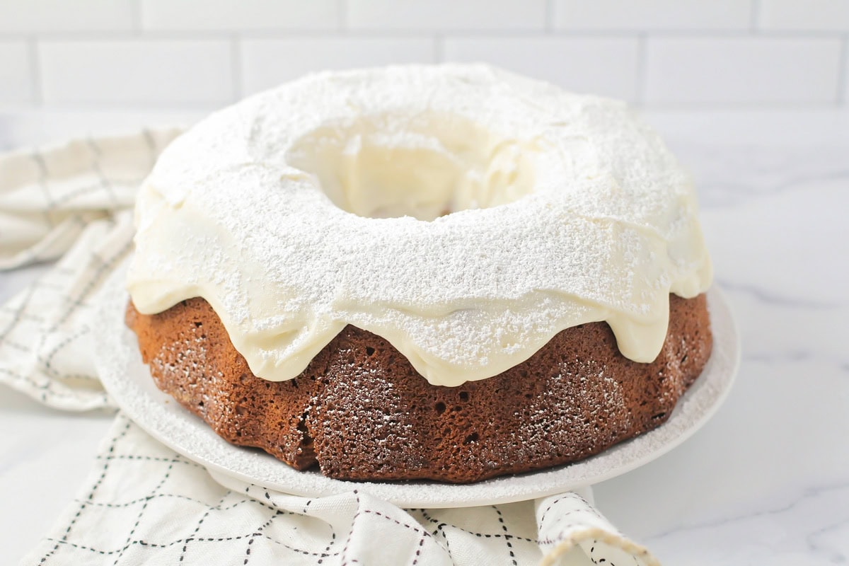 A frosted pumpkin bundt cake topped with frosting and powdered sugar.