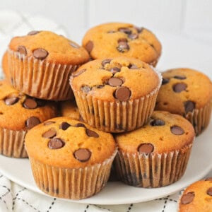 Several pumpkin chocolate chip muffins stacked on a white platter.
