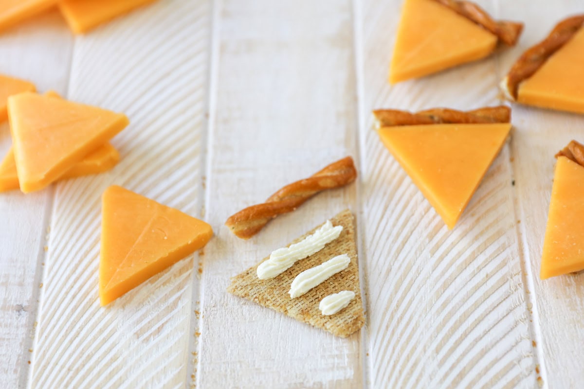 Piping cream cheese onto a triscut cracker.