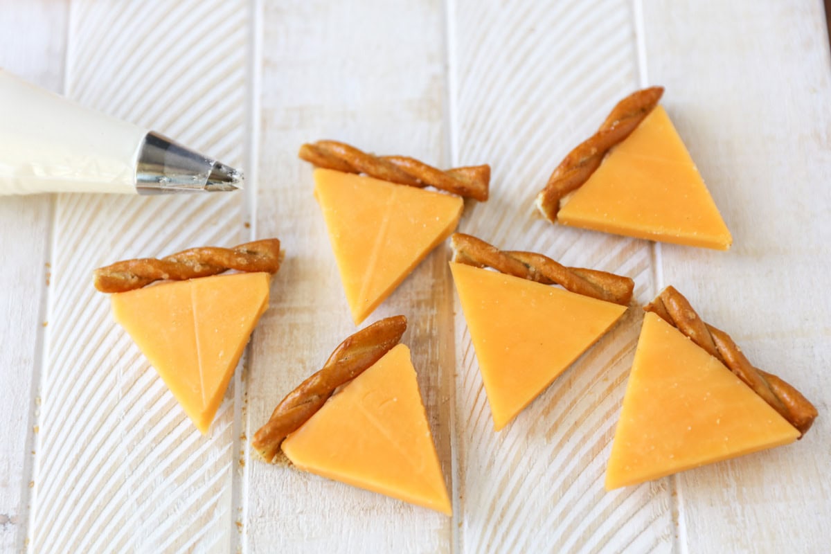 Adding cheese and pretzel to the top of a cracker with cream cheese.