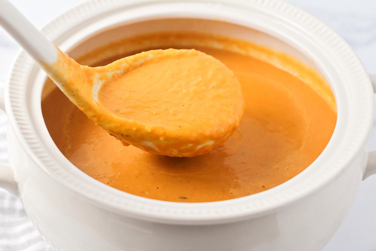 Pumpkin soup being spooned from a small white bowl.