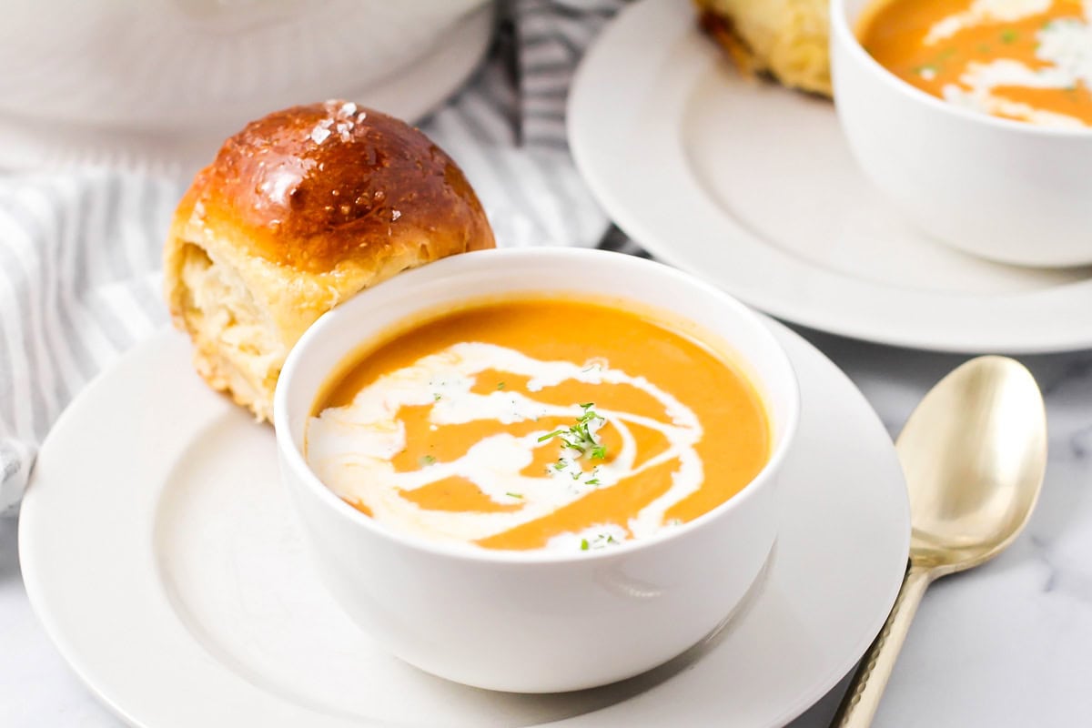 Pumpkin soup with a swirl of cream served with a roll.