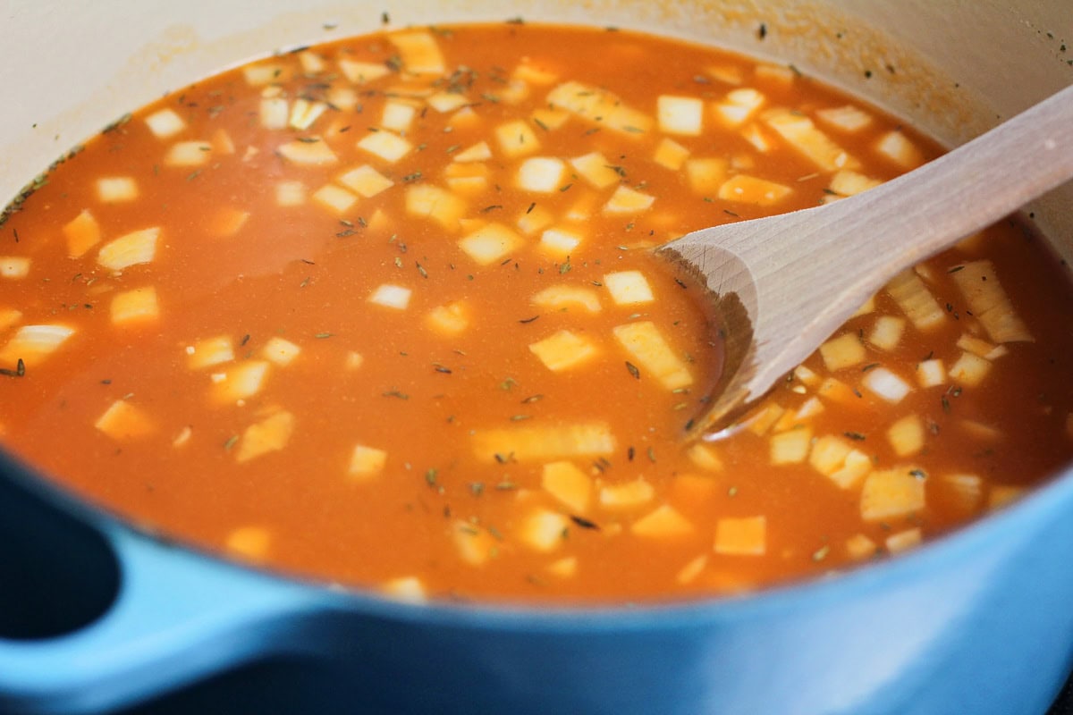 Broth, onion, spices, and pumpkin puree in a pot on the stove.