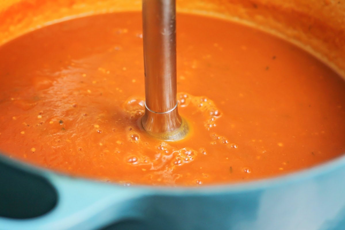 An immersion blender blending soup in a pot.